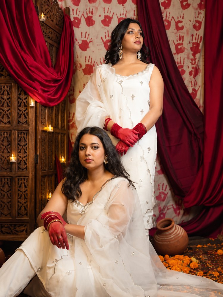 Two women in ivory organza kurti sets with scalloped, sequinned edges, against red drapes